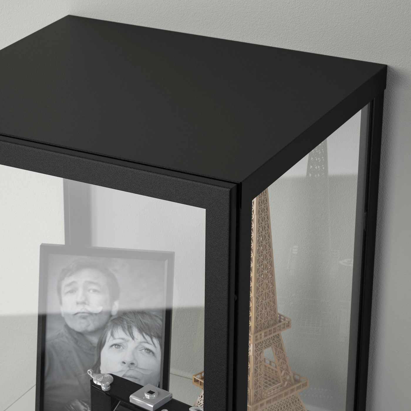 Schwarze IKEA Vitrine mit Glastür, darin persönliche Erinnerungsstücke wie ein gerahmtes Foto, ein Miniatur-Eiffelturm und Schmuck – stilvolle Aufbewahrung für Sammlerstücke und Dekoration.