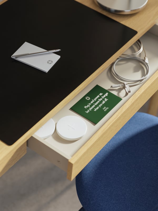 TONSTAD radni sto od hrastovog furnira s otvorenom fiokom. Unutra su bežični punjači, USB kablovi i napomena.