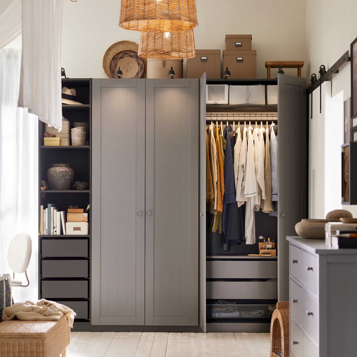 A bedroom with a PAX/GULLABERG wardrobe combination with hanging clothes, boxes above and decoratibve items on an open shelf.