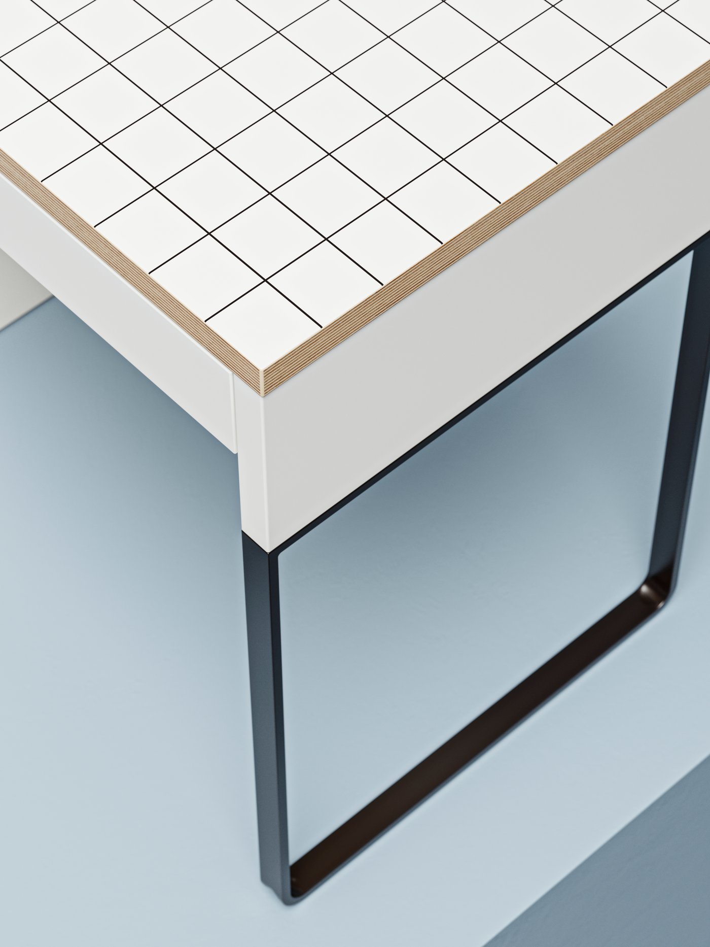 A section of a light MICKE desk, its top decorated with a geometric monochrome pattern and the legs a contrasting dark shade.