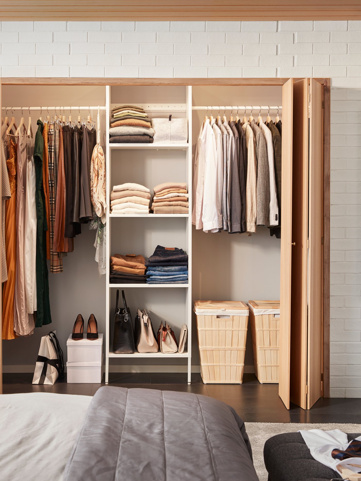 A tidy bedroom AURDAL closet next to a bed, filled with clothes, shoes, and laundry baskets.