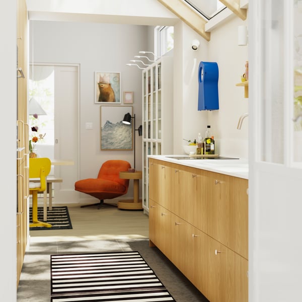A kitchen with a dining area in the background has SINARP fronts in oak veneer and a black and white striped ELSYSTEM rug.