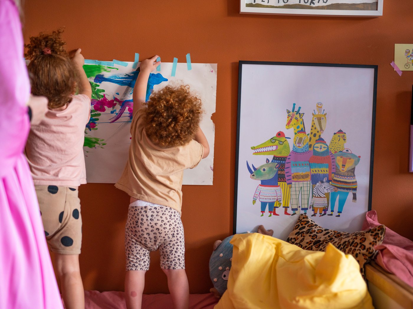 Children taping a drawing on the bedroom wall next to other artwork.