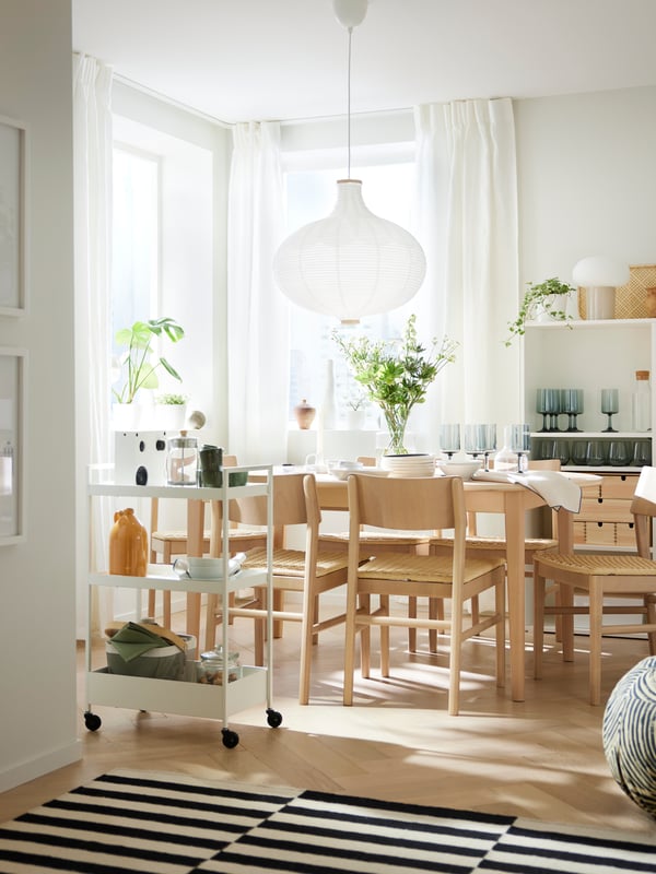 NISSAFORS kolica stoje blizu SKANSNÄS okruglog produživog stola od svetle bukovine/furnira i nekoliko SKANSNÄS stolica od svetle bukovine.