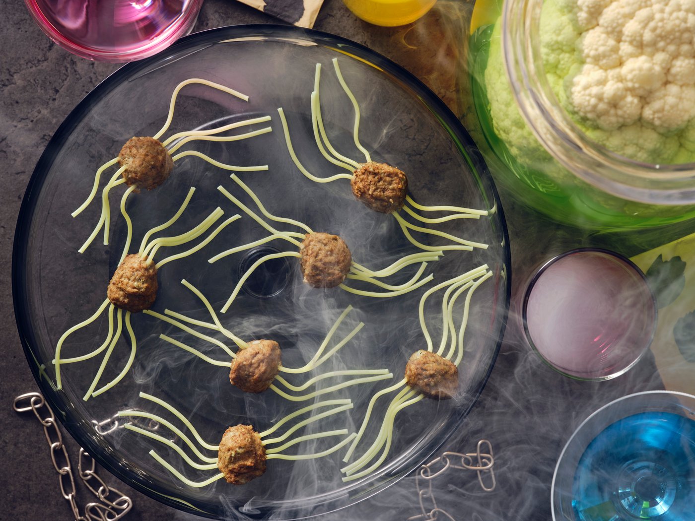 Spider meatballs made with HUVUDROLL plantballs or meatballs and spaghetti for legs laid on a black plate with smoke.