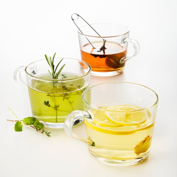 Three IKEA 365+ mugs in clear glass. One with brown tea, one with green tea and rosemary, and one with yellow tea and lemon.