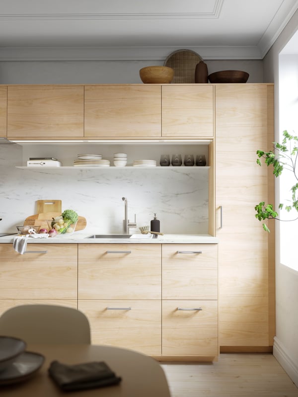 A METOD kitchen with wooden fronts and doors, chrome handles and white marbled splashbacks. Tableware on an open shelf.