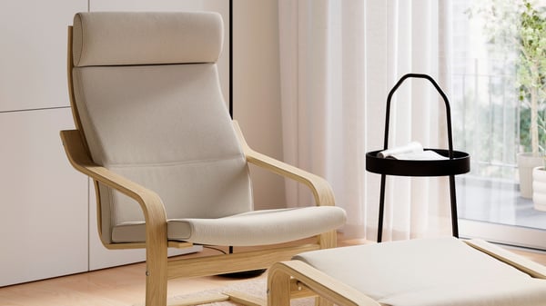 An oak/Kelinge beige POÄNG armchair and footstool and a black side table in a bright living room.