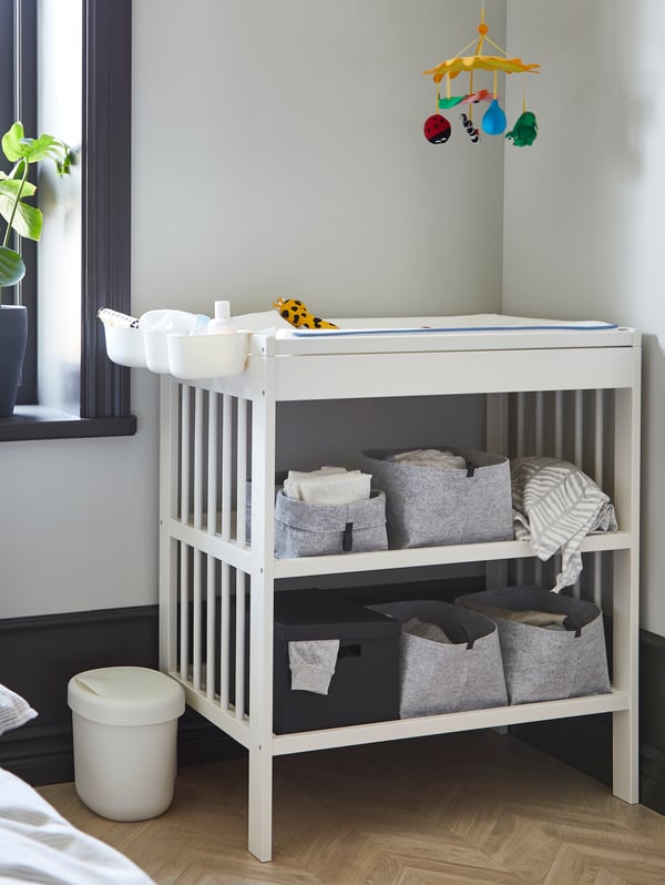 A GULLIVER changing table with RAGGISAR baskets on its shelves stands in a corner under a colourful KLAPPA mobile.