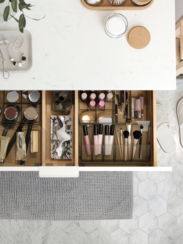A wash-stand in a white marble effect. A drawer is open revealing beauty products neatly organised in GODMORGON boxes.