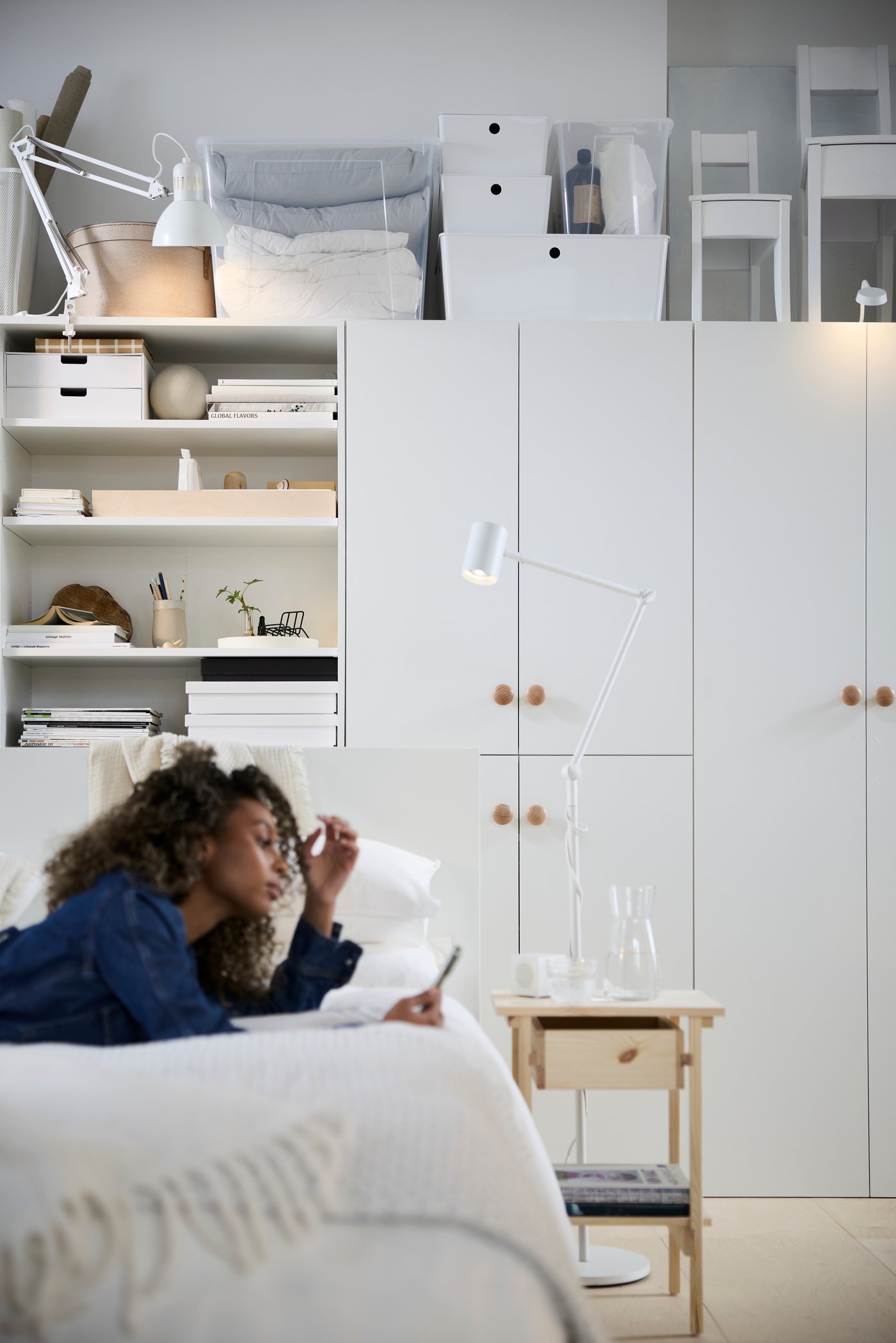 A person relaxes on a bed in a multifunctional living space with white cabinets and shelves.
