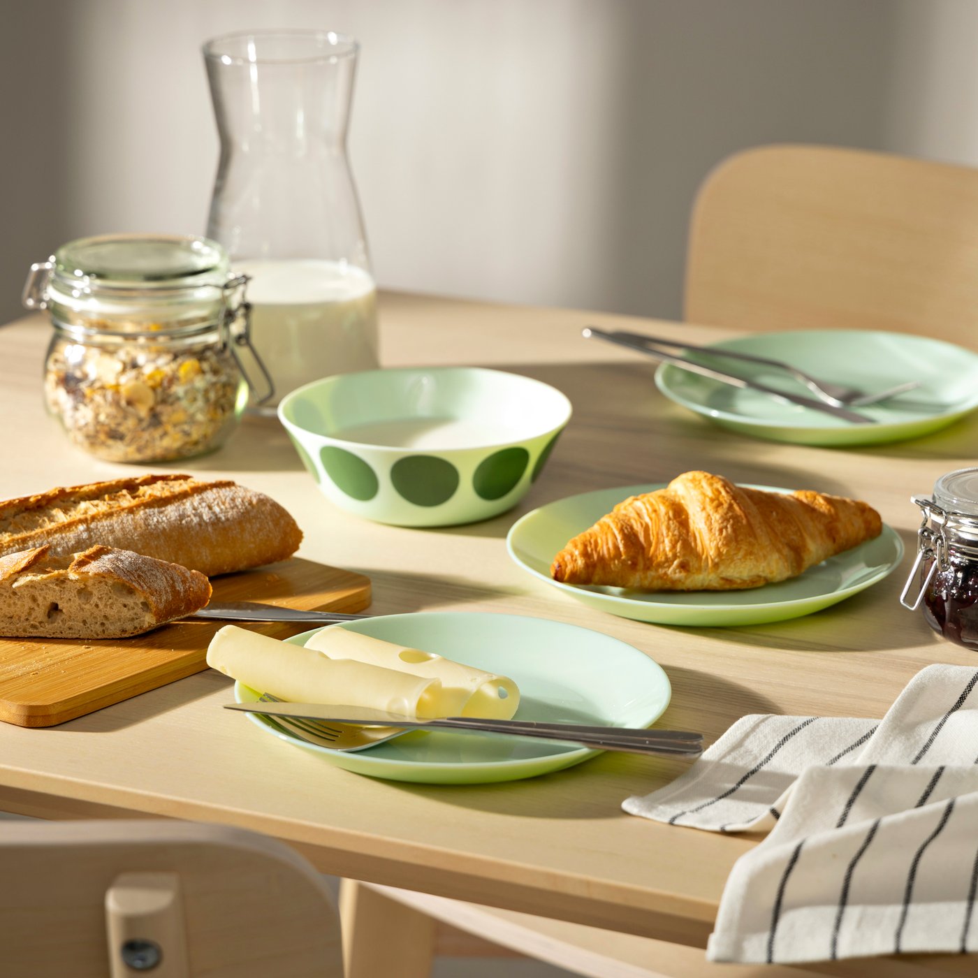 Una mesa de madera con desayuno donde destacan platos de pan OFTAST verdes.