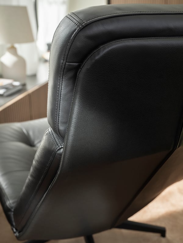 The back and upper corner of a black-leather HAVBERG swivel armchair, placed on a light floor, facing sunlit windows.