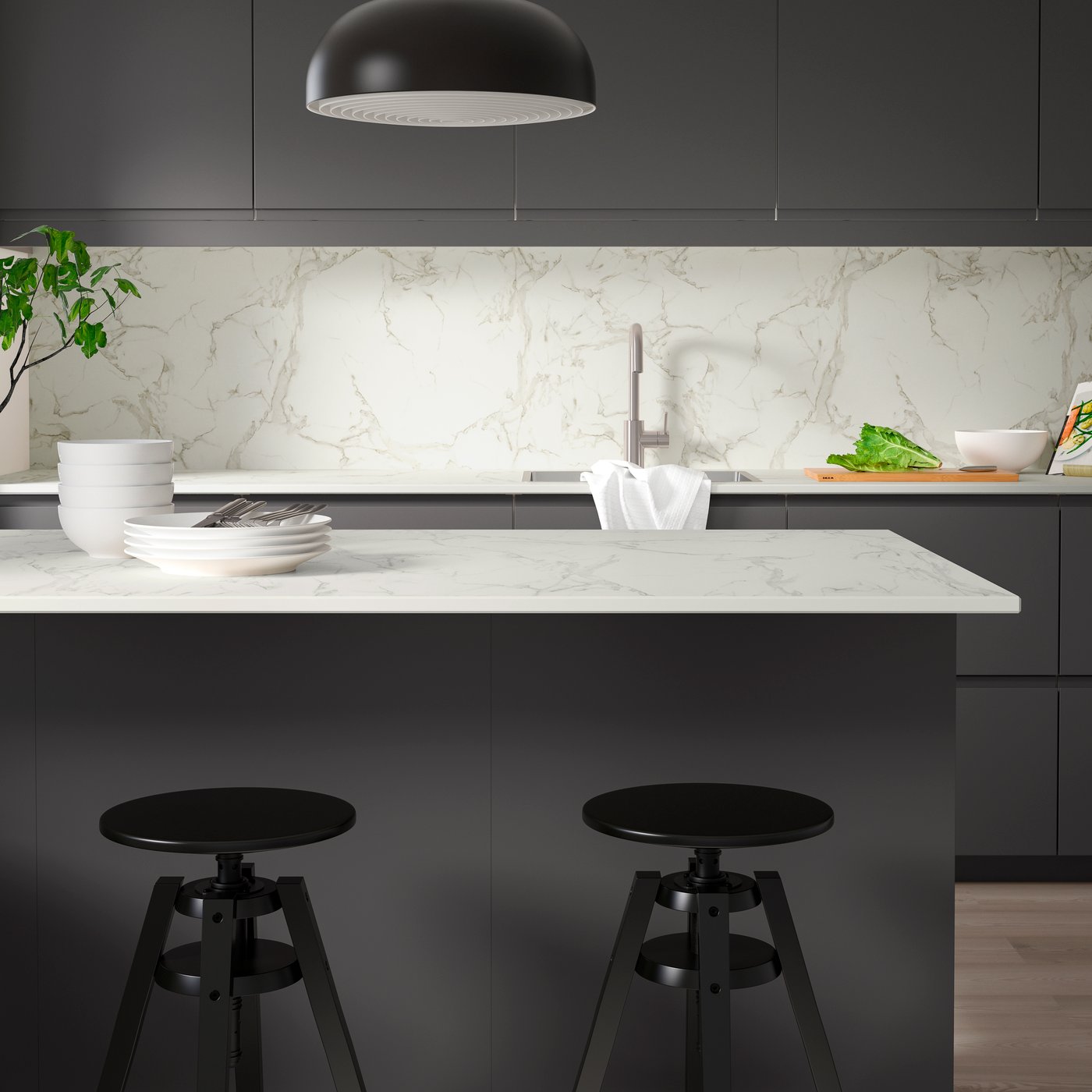 A kitchen with RUNSBÄCK custom-made worktop in white/grey on the kitchen island, tableware, and two black kitchen stools.