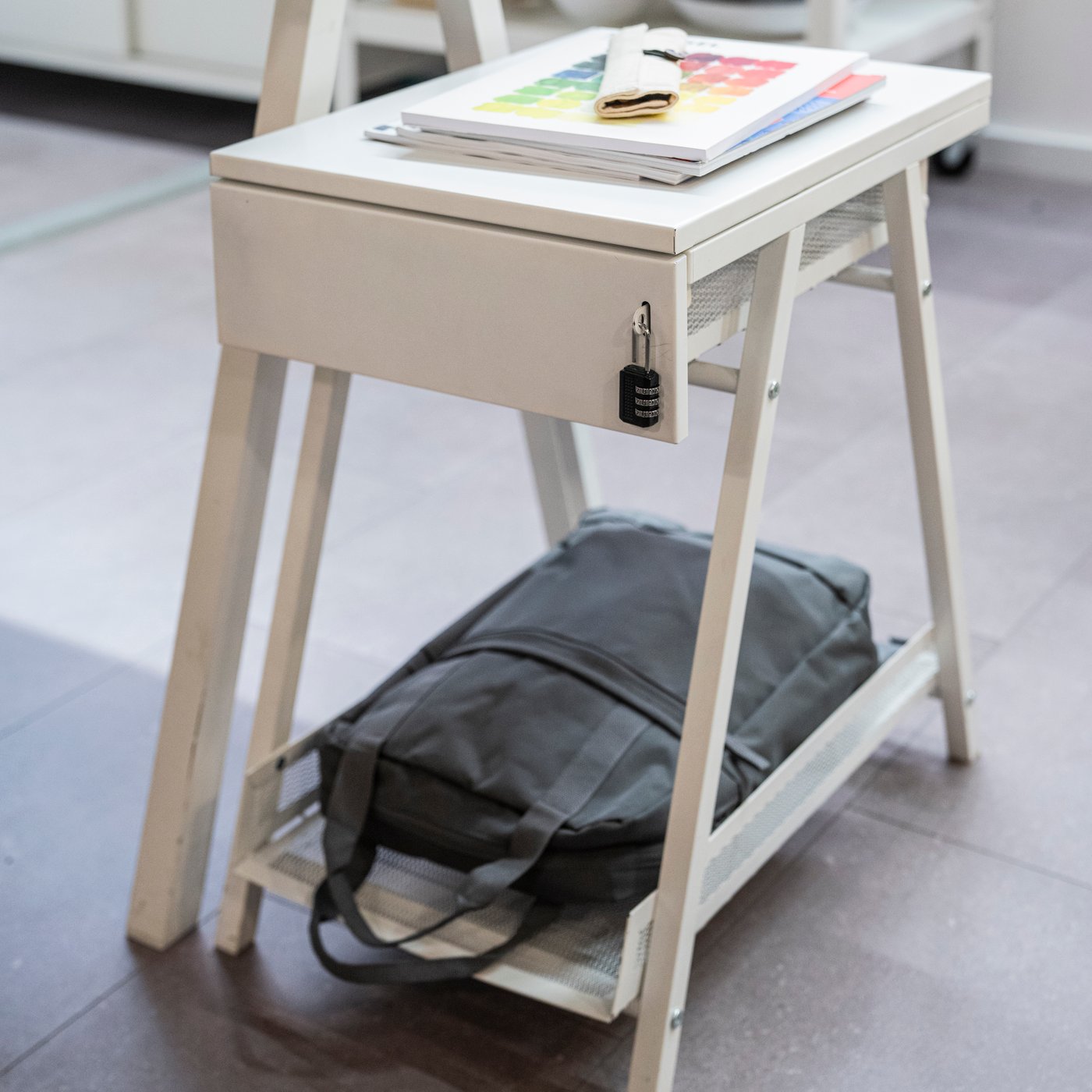 Un bureau blanc sur lequel est posé un sac à dos gris dans un compartiment inférieur. 