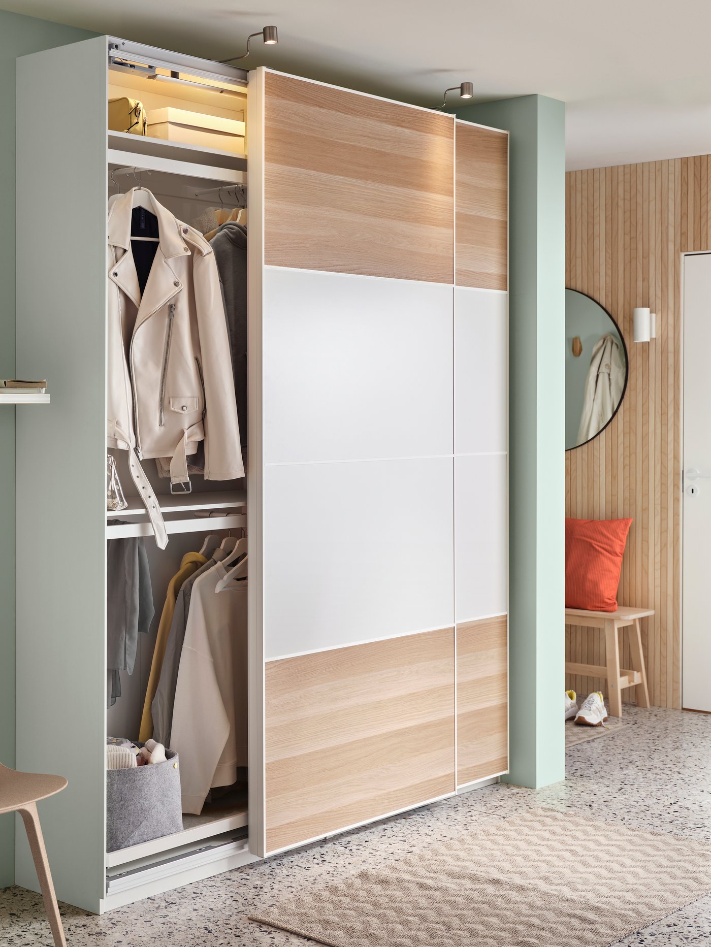 A wardrobe in light wood filled with clothes on shelves but also hanging on hangers.