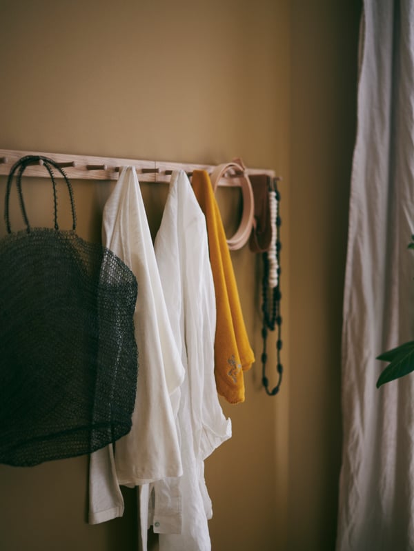 Clothes, a bag and various accessories in diverse colours hanging from a HÖVOLM rack with 6 knobs.