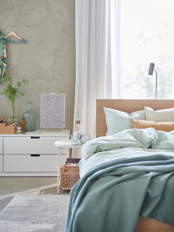 A light bedroom with an air purifier and plant sitting on the nightstand.
