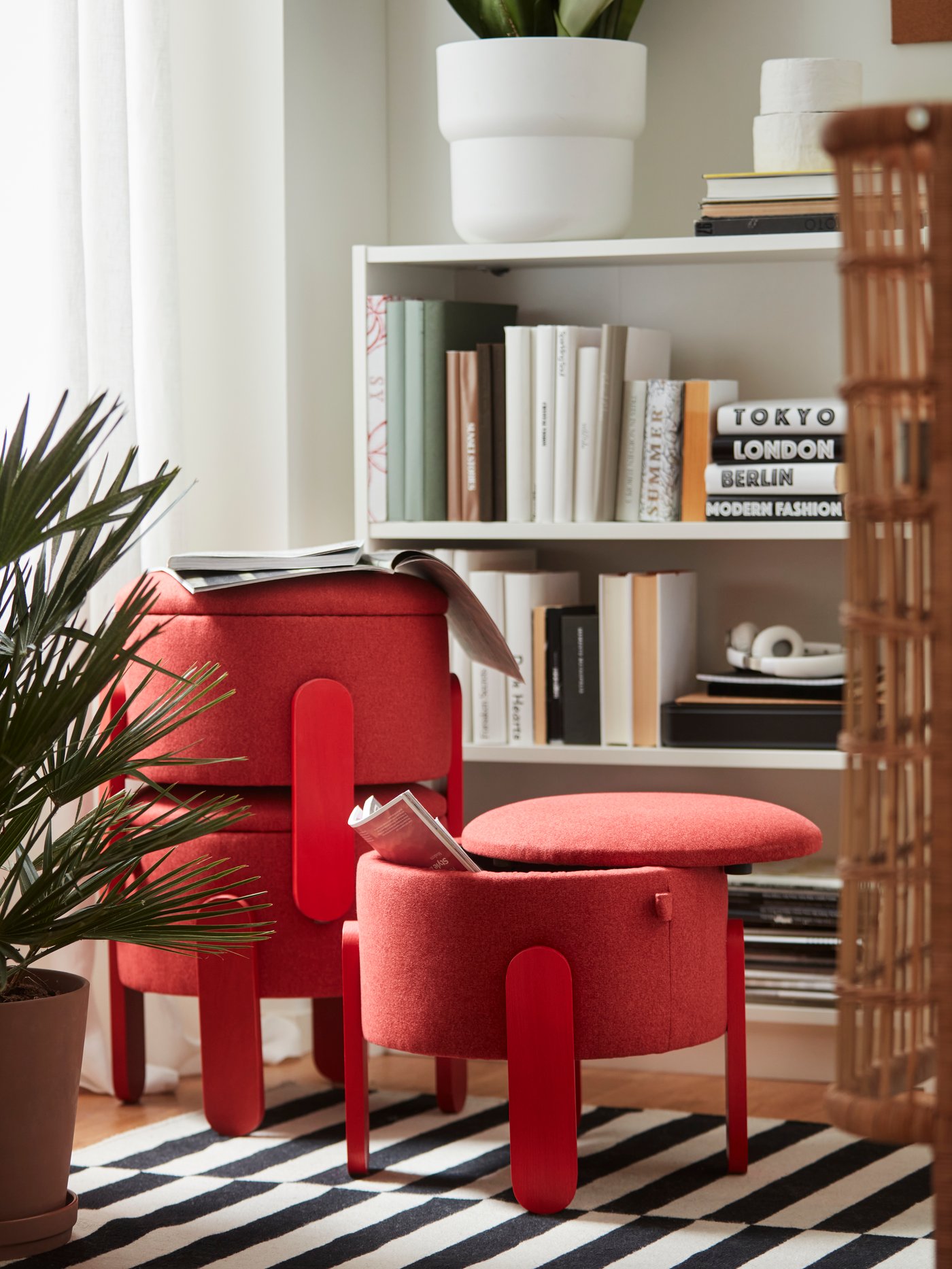 Three red FÖRLUNDA pouffes with storage stand on a striped rug in a living room. One pouffe is stacked on top of another.