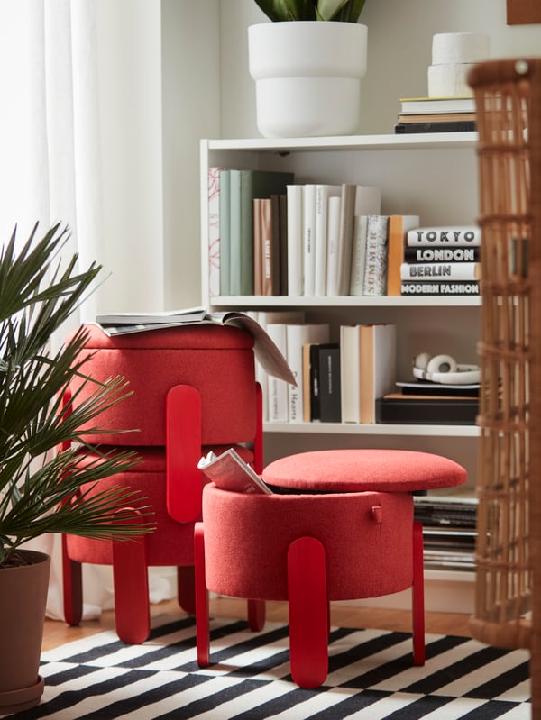 Three red FÖRLUNDA pouffes with storage stand on a striped rug in a living room. One pouffe is stacked on top of another.