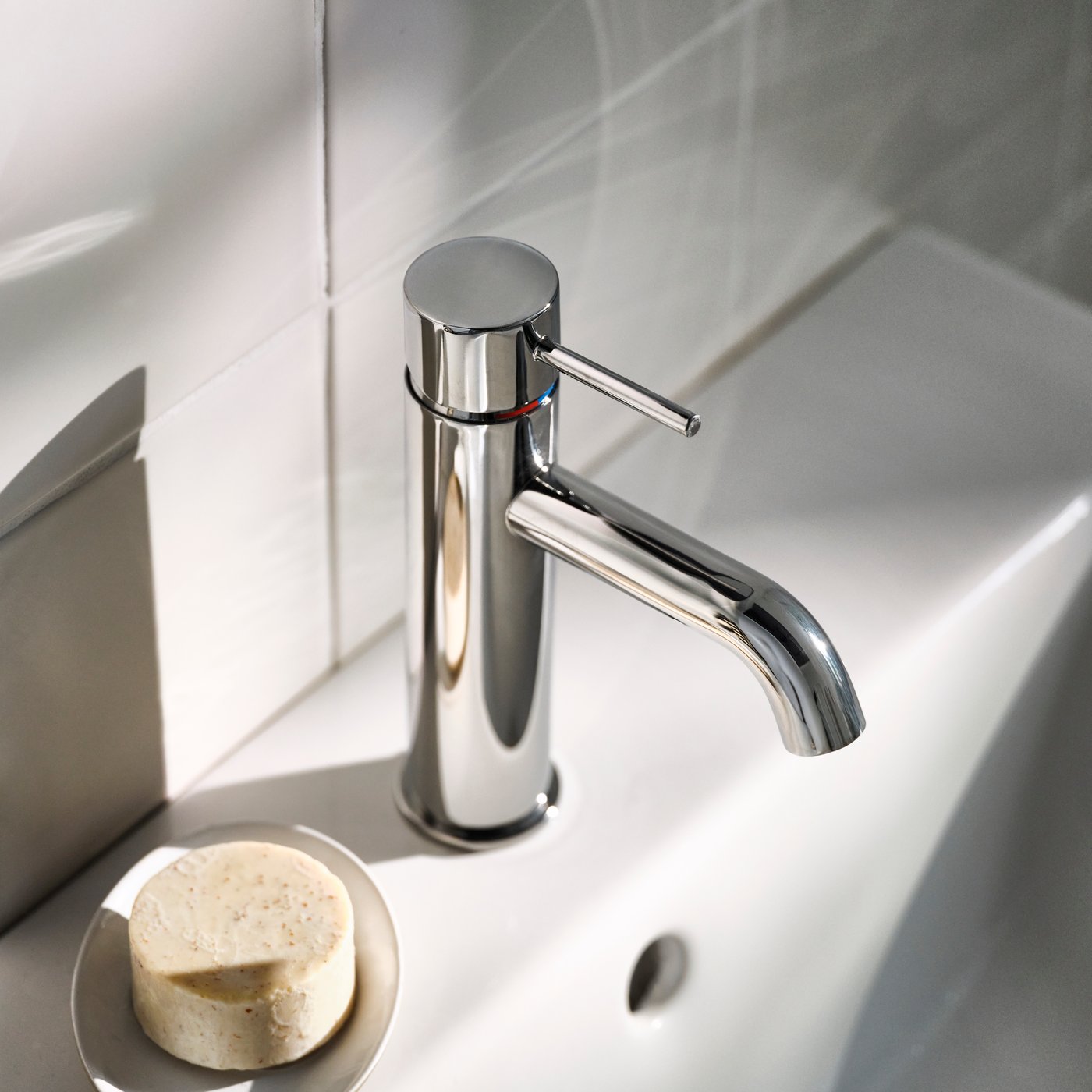A close-up of a SALLSJÖN bathroom mixer tap with a top lever beside a round soap dish and bar.