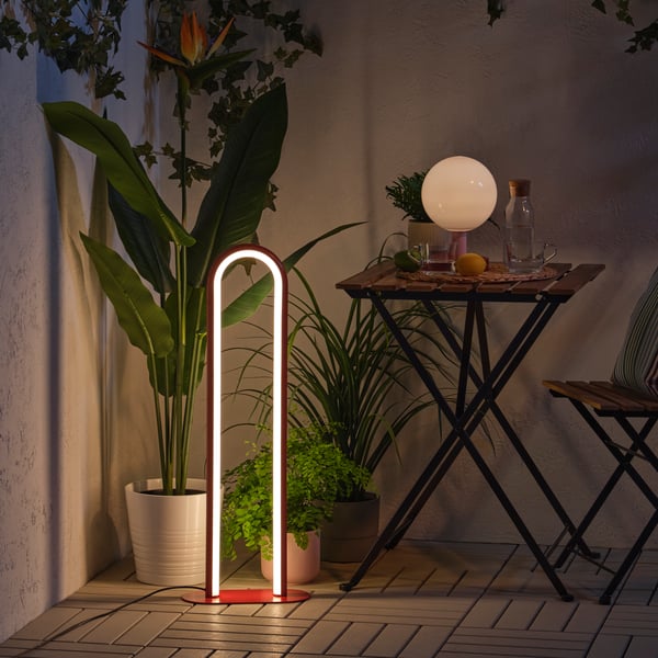 A dimmable red SOLVINDEN floor lamp creates a snug mood in the dark, surrounded by green plants and a balcony table.