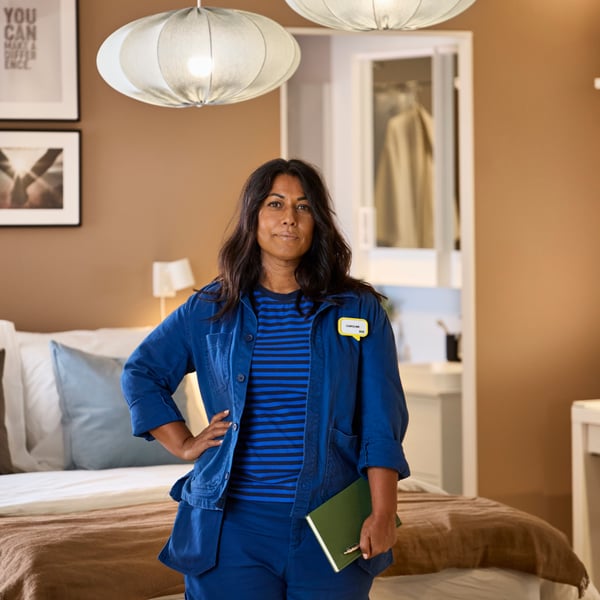 An IKEA interior designer in her blue work uniform standing in a showroom holding a notebook.