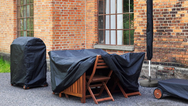 A black TOSTERÖ parasol, garden table and barbecue cover outside in the garden. Protect your garden furniture with a TOSTERÖ cover.