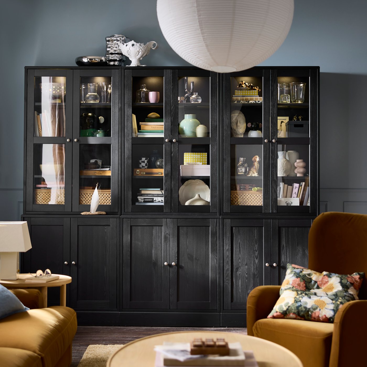 Una sala de estar con una combinación de almacenamiento HAVSTA negra con puertas de vidrio, que exhibe objetos decorativos y libros.