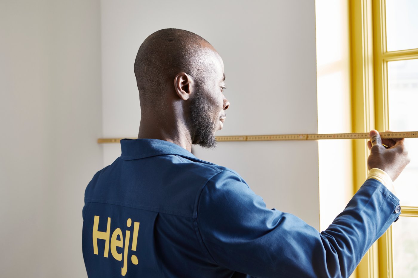 En mand i IKEA-uniform måler en væg.