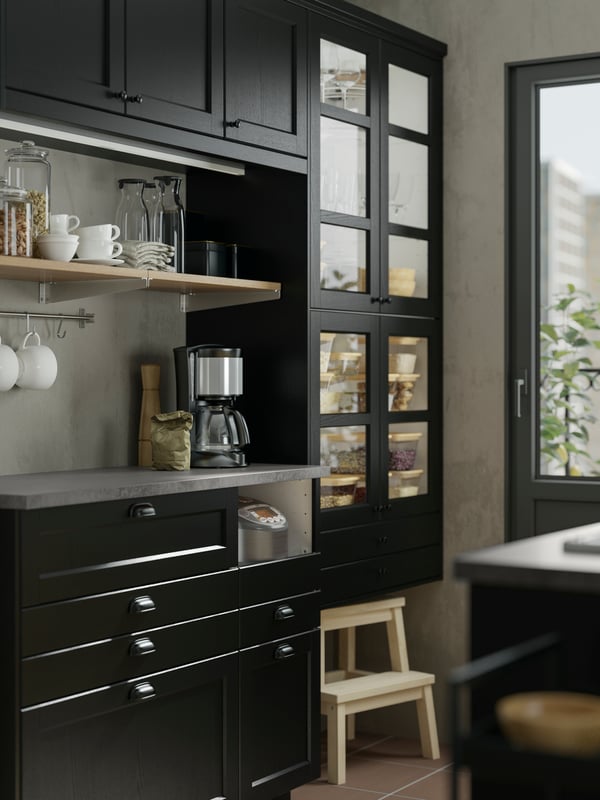 Dapur ala tradisional yang mempunyai bahagian hadapan dapur LERHYTTAN berwarna hitam. Cawan tergantung pada rel di bawah para.