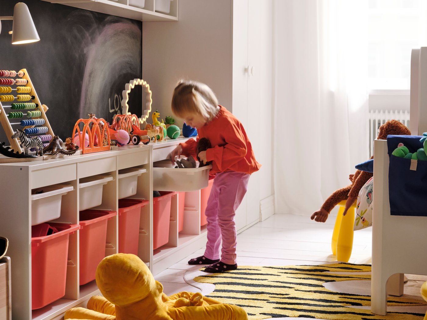 Dans une chambre d’enfant, une fillette farfouille dans l’un des bacs d’une longue combinaison de rangement installée le long du mur.
