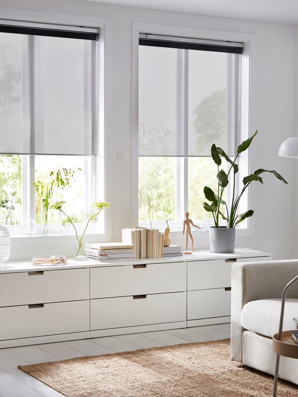 A living room with two KADRILJ roller blinds, half-way down, in two windows above three low chests of drawers.