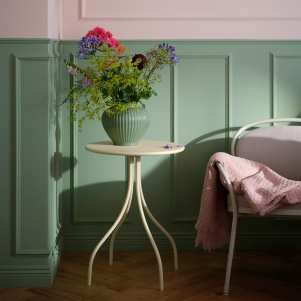 A pale yellow TÅNEBRO side table holds a vase of flowers next to an armchair in a softly lit, green-walled room.