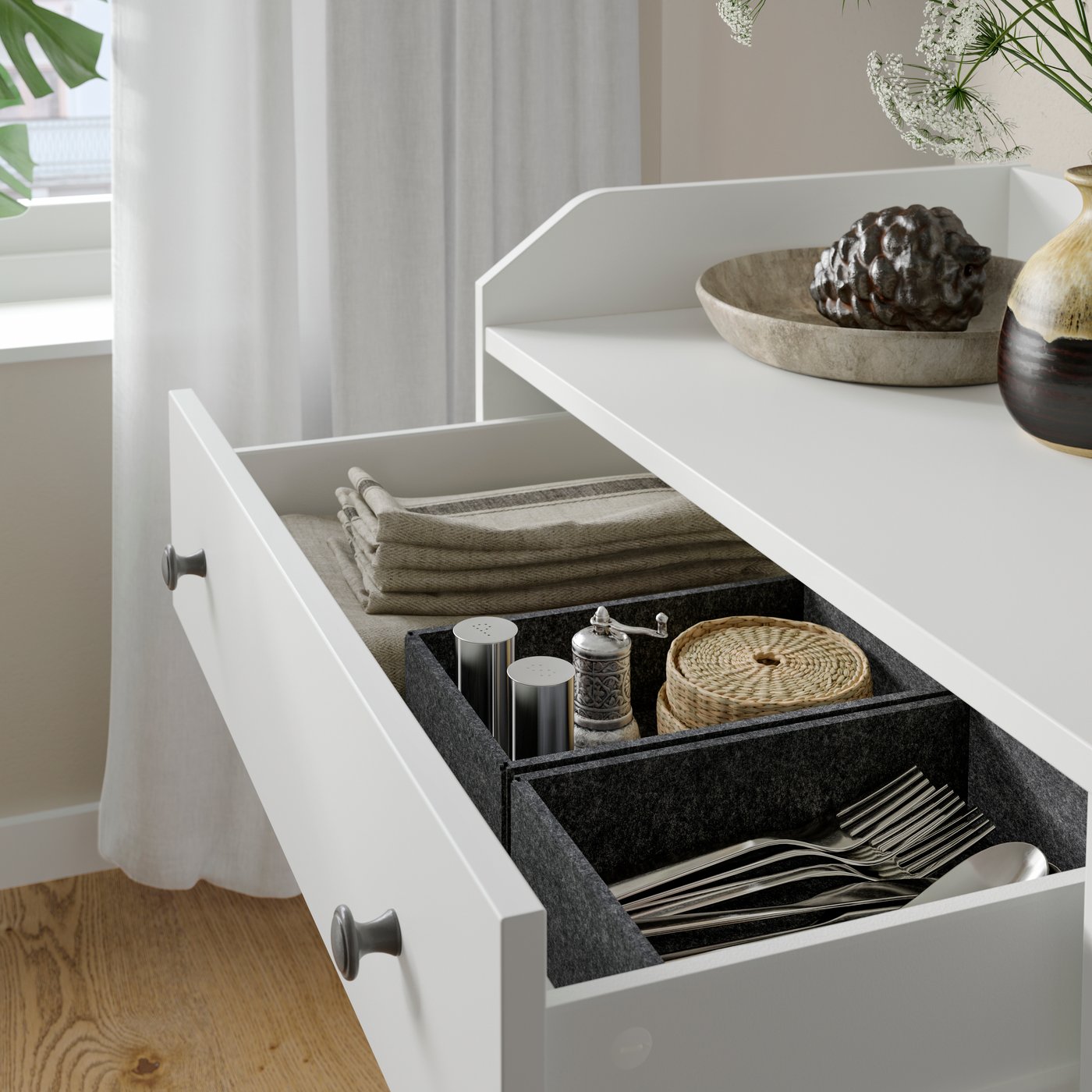 Tiroir ouvert d’une commode 6 tiroirs HAUGA blanche contenant des serviettes en tissu pliées, des sous-verres et des couverts.
