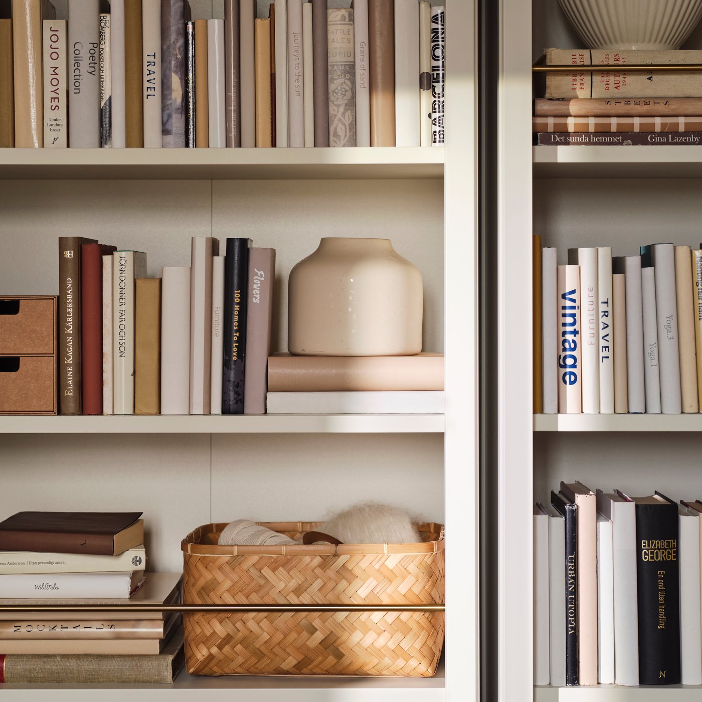 A close-up of two off-white FÄRJKARL bookcases with books, a BLODBJÖRK vase and a bamboo MJÖLKKANNA basket on the shelves.