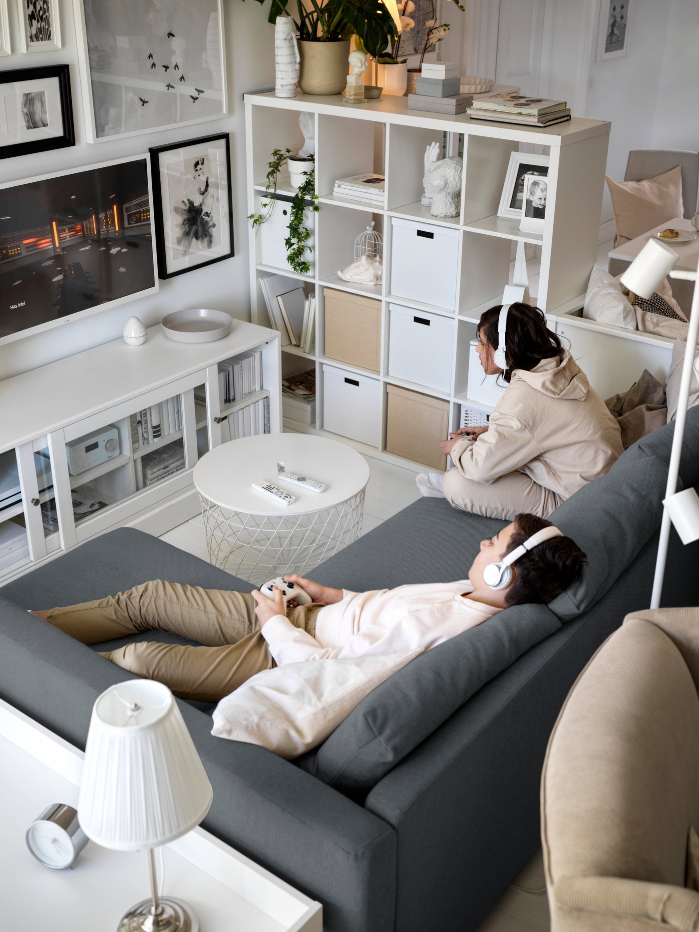 Two children sat on a grey corner sofa bed play a video game on a TV mounted above a white HAVSTA TV bench with plinth.