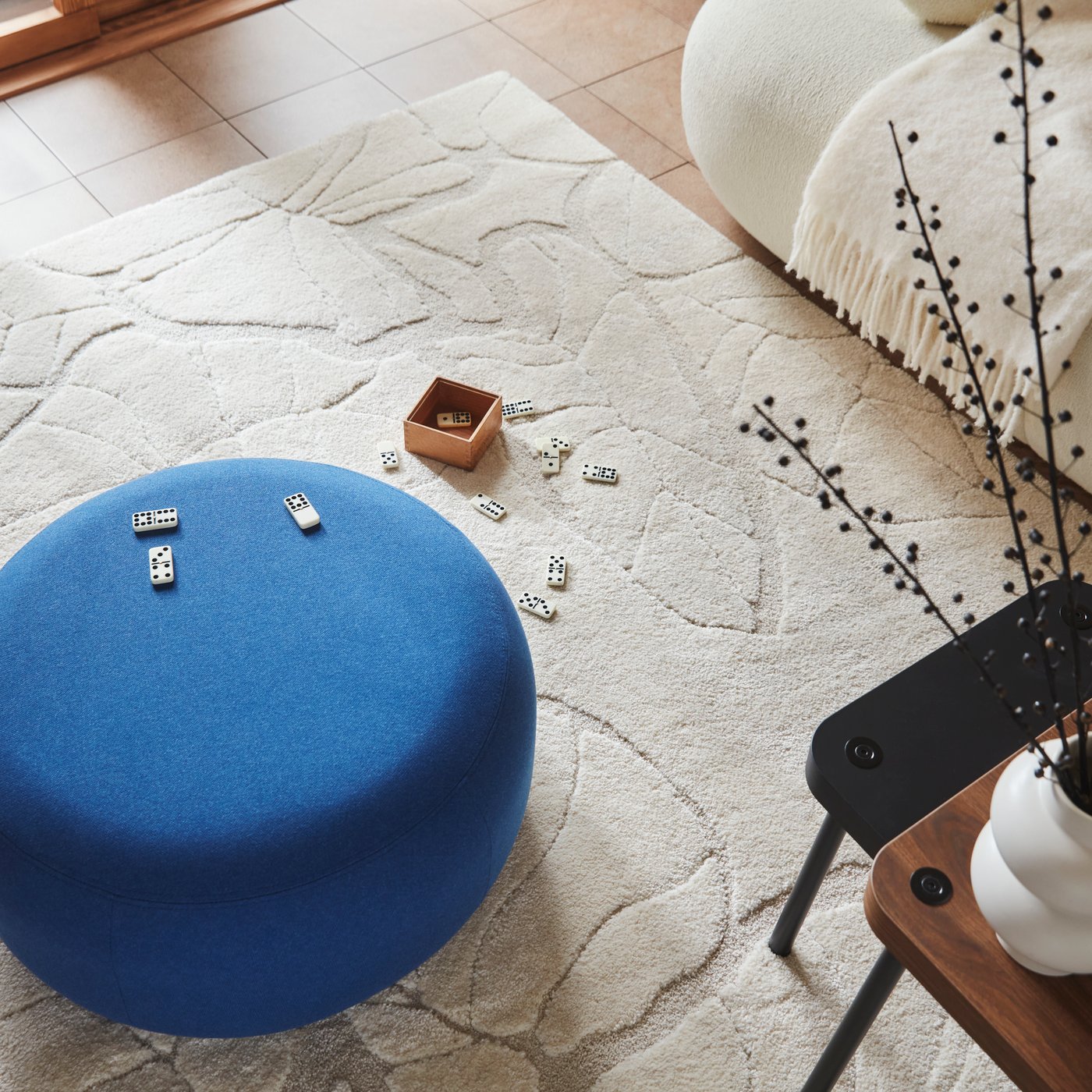 A living room featuring a Gunnared dark blue LILLESÄTER pouffe placed on a light beige PELARKÖRSBÄR low pile rug.