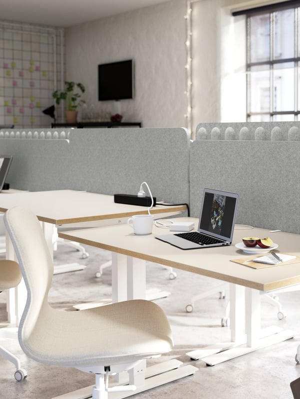 Several white desks and beige/white chairs grouped together and separated with light grey screens between the desks.