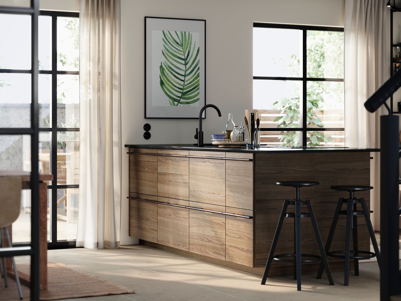 A kitchen island with STENSTA dark brown ash veneer fronts, complemented by bar stools and a large plant print on the wall.