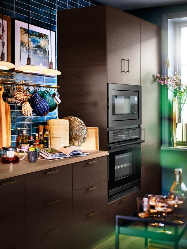 A kitchen with SEKTION cabinets, a SÄLJAN countertop in oak effect laminate, TÄLLBYN pendant lamps and kitchen items hanging.