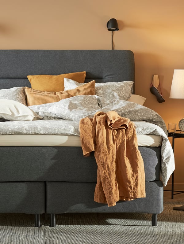 A grey FINNSNES divan bed with JÄTTEVALLMO bed linen in white/grey stands in a bedroom with yellow walls.