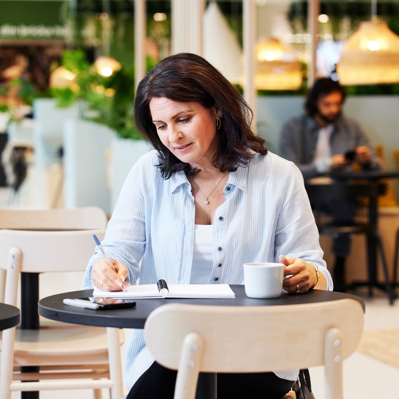 A woman sits taking notes in her notepad, with a coffee cup in her hand.