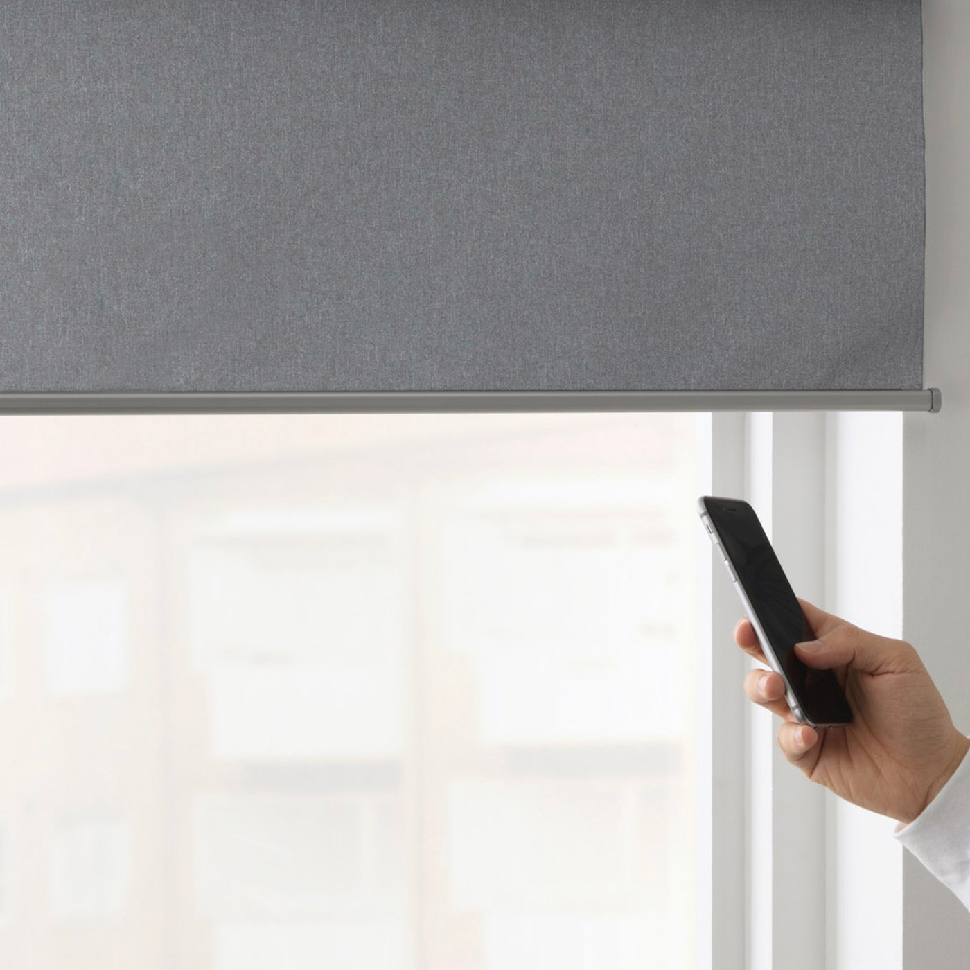 Osoba drži mobilni uređaj s aplikacijom IKEA Home smart i podešava položaj FYRTUR pametne roletne. 