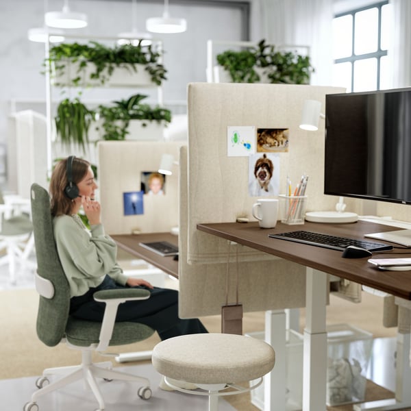 A dynamic workspace with a LIDKULLEN sit/stand support and a women in a GRÖNFJÄLL office chair in Letafors grey-green/white.