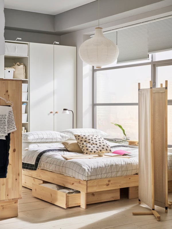 Recámara en tonos beige con cama, clóset y separador de ambientes GLAMBERGET de madera natural. De fondo, un clóset blanco y una ventana.