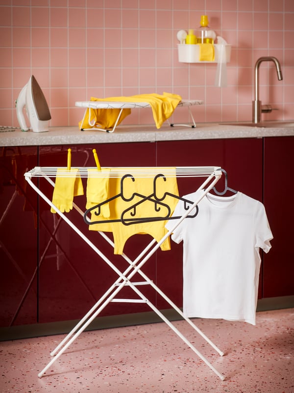 Laundry room with a drying rack, tabletop ironing board and iron, with yellow clothes and textiles on the drying rack and ironing board.