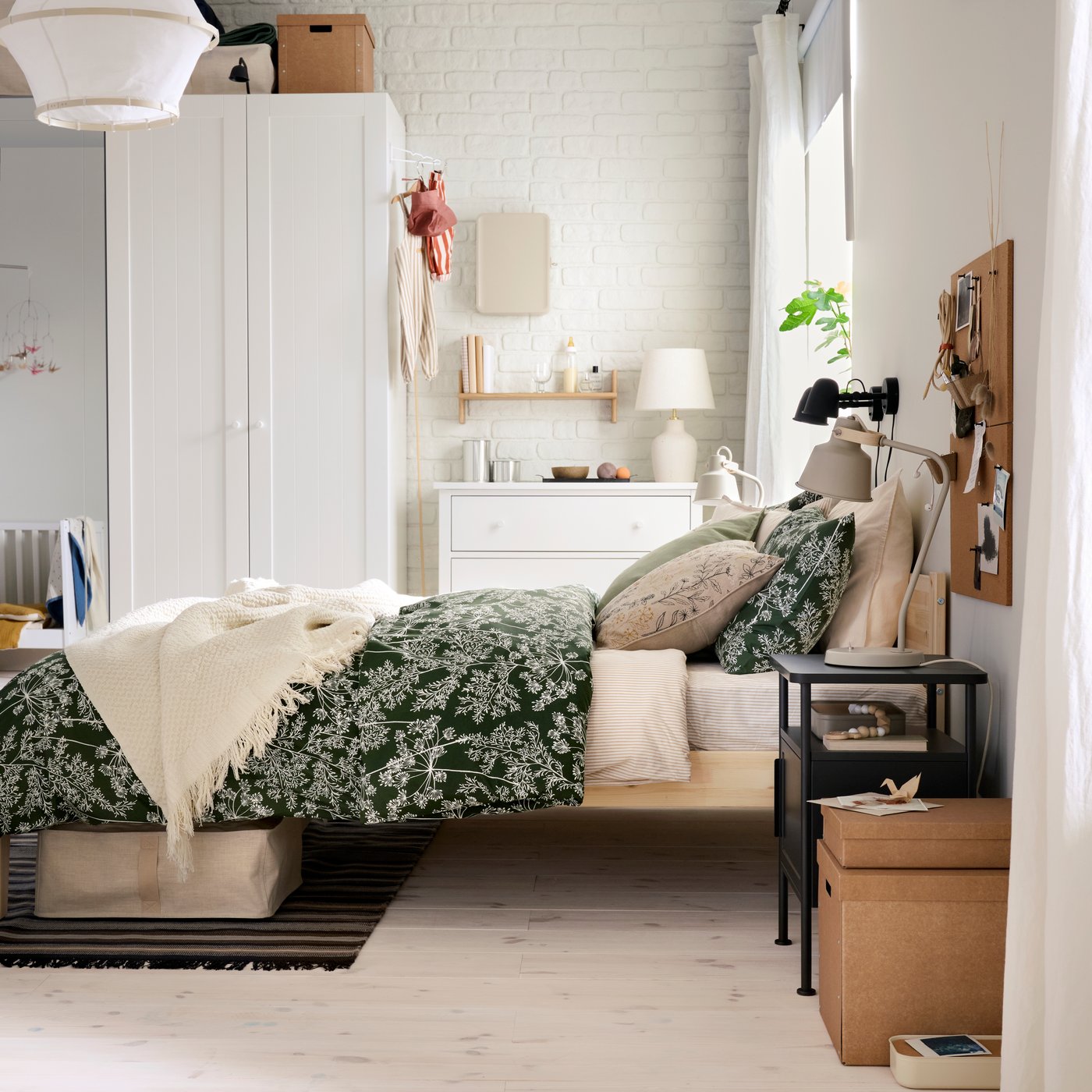 Un dormitorio luminoso con una cama TAXÅSKLINT de madera, un edredón de flores y un armario PAX blanco en el fondo.