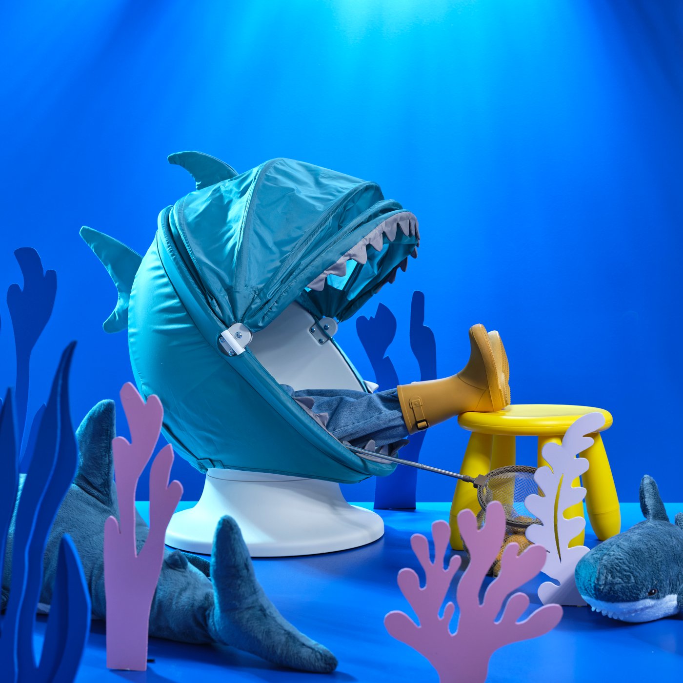 طفل يجلس على كرسي دوار IKEA PS LÖMSK بذراعين مع غطاء قماشي بشكل القرش. كرسي صغير MAMMUT، ألعاب طرية BLÅVINGAD على الأرض.