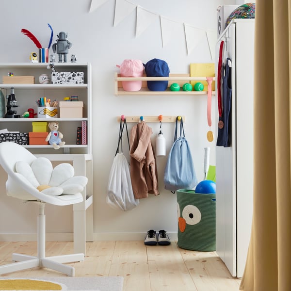 Ein Kinderzimmer mit einem FLISAT-Knopfregal mit vier bunten Knöpfen, an denen Aktivitätentaschen und Kleidung unter einem Wandregal aufgehängt sind.